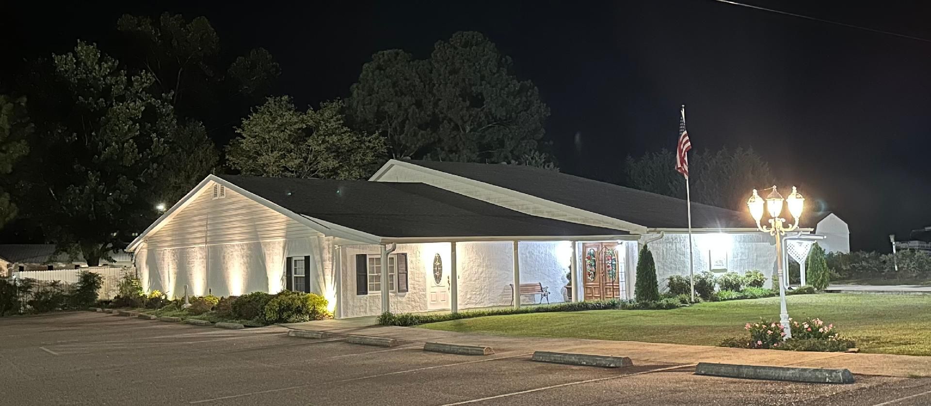 Well-lit single-story house at night with a lit porch and yard lamps on a quiet street.