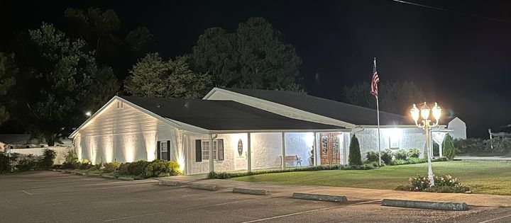 Well-lit single-story house at night with a lit porch and yard lamps on a quiet street.