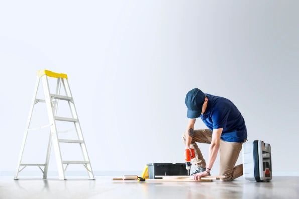 A man is kneeling on the floor using a drill.