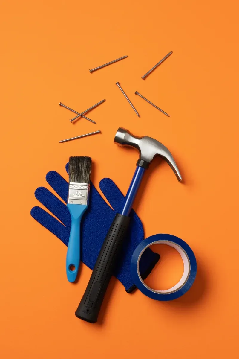 A hammer , brush , tape and nails on an orange background.