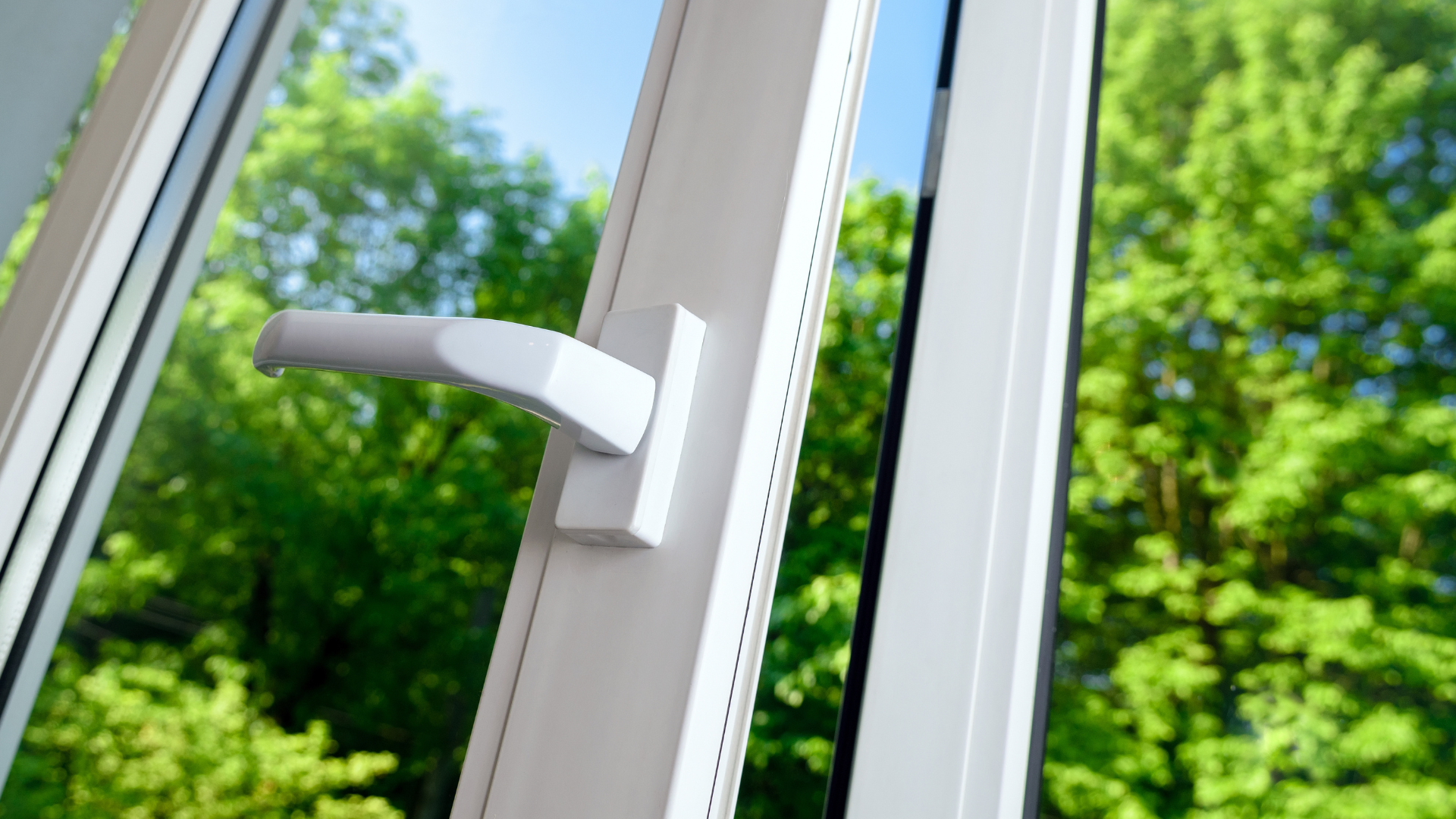 White window with handle open, showing green trees outside.