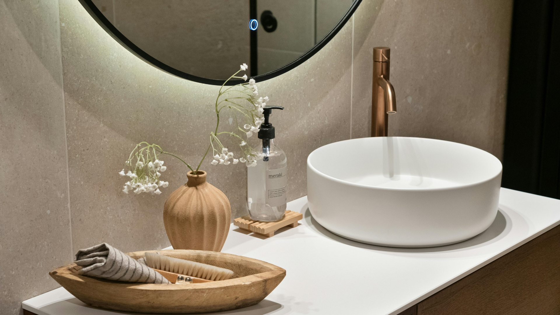 Bathroom sink with a copper faucet, round mirror, and decorative elements on the countertop.