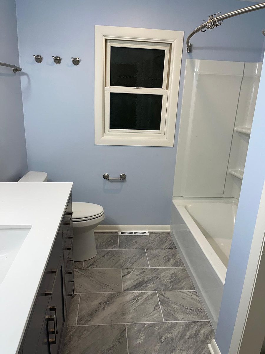 A bathroom with a toilet , sink , bathtub and window.