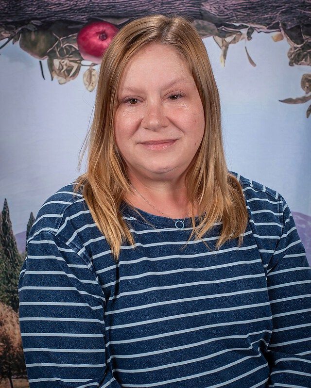Portrait of a smiling woman in a blue striped shirt against a light blue backdrop with dried flowers above