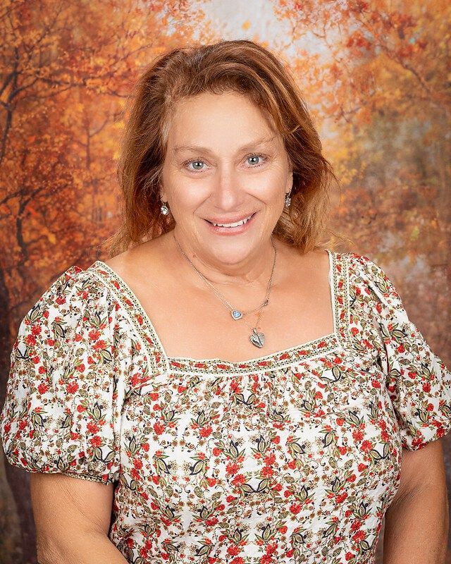 Smiling woman in floral blouse posing before an autumn-colored backdrop
