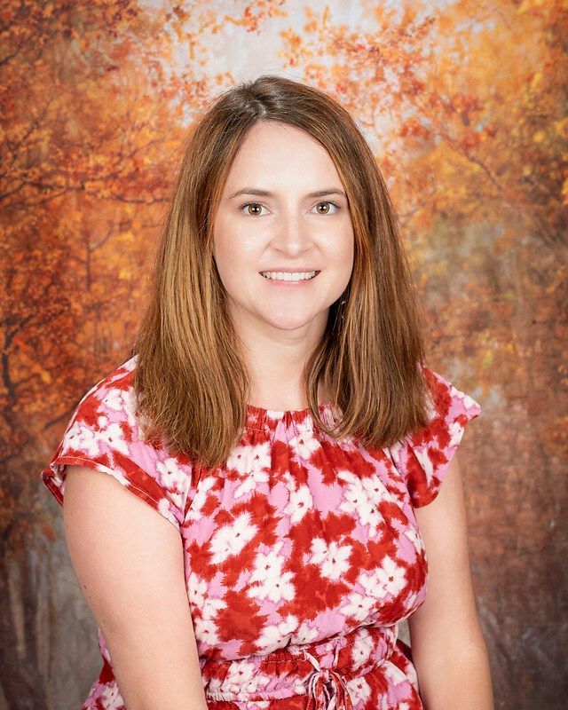 Woman in a red floral dress smiling against an autumn-colored backdrop