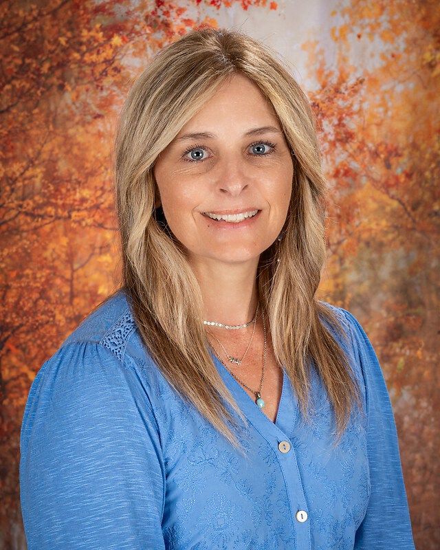 Smiling woman in a blue shirt against an autumn-toned backdrop