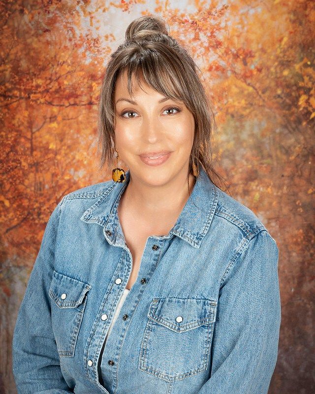 Portrait of a smiling woman in a denim shirt against an autumn-themed backdrop