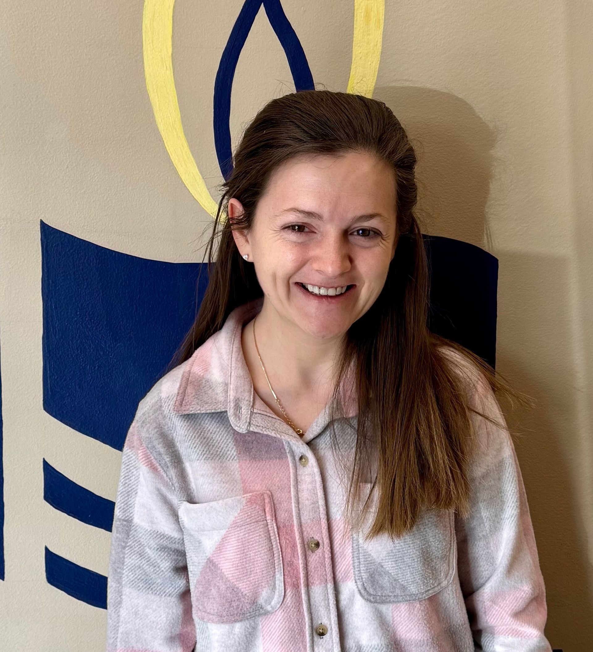 Smiling woman standing indoors before a wall with abstract blue and yellow shapes