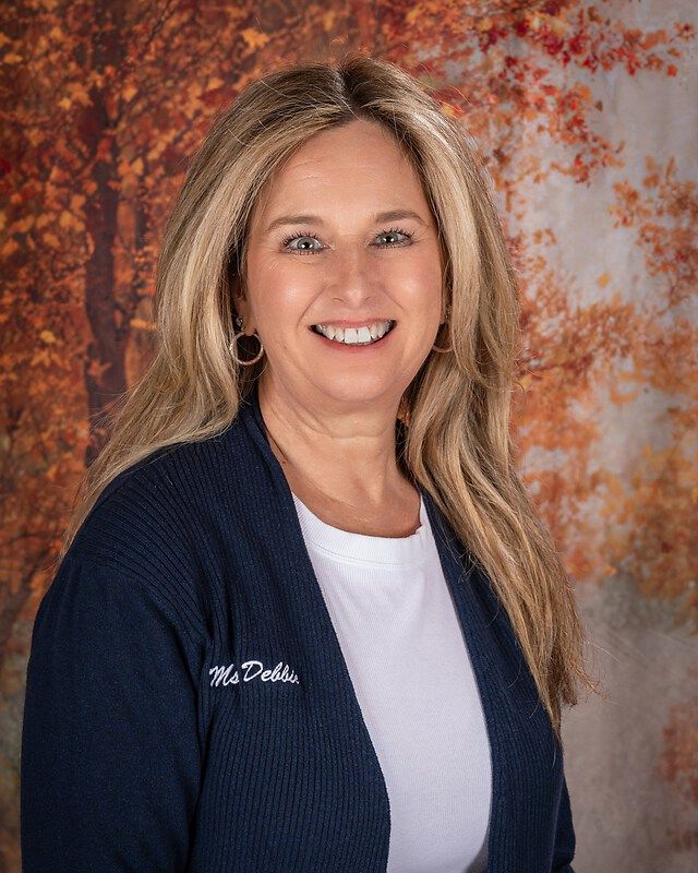 Smiling woman in a navy cardigan and white top against a warm autumn-themed backdrop