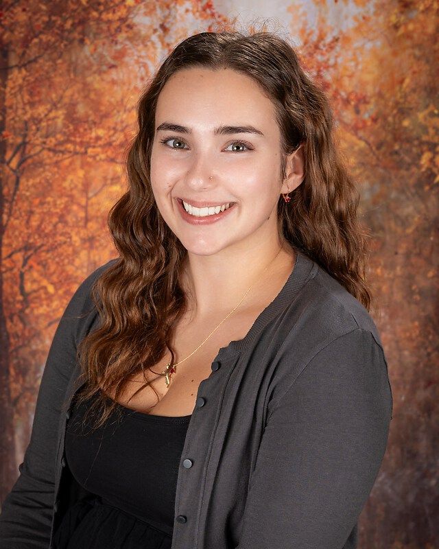Smiling woman in a dark top against an autumn-colored studio backdrop