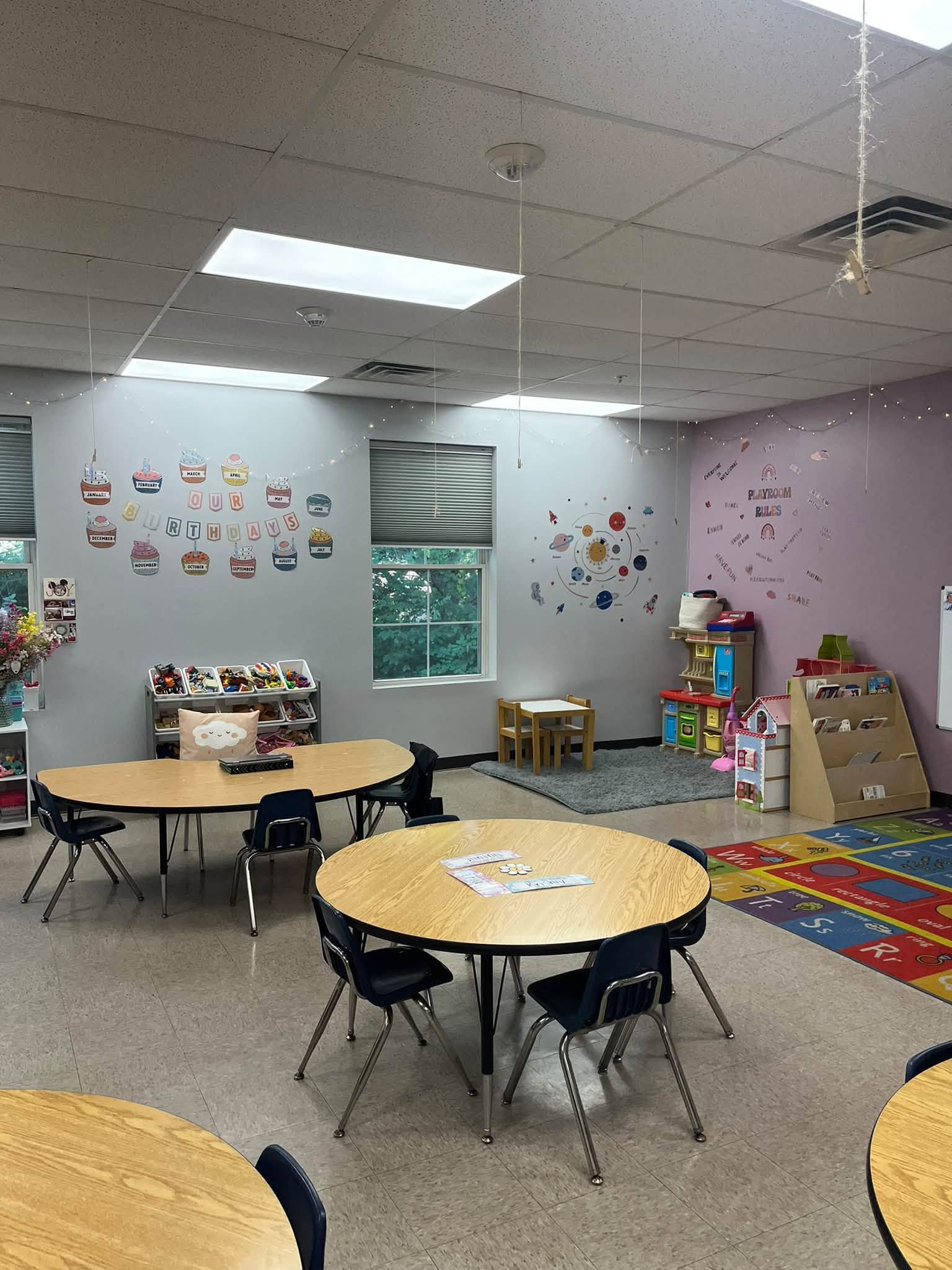 Children and a teacher coloring at a table in a sunny classroom, with books, cross, star decorations, and globe.