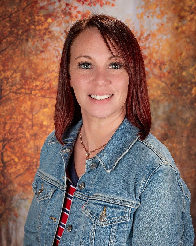 Smiling woman in denim jacket against a warm orange studio backdrop