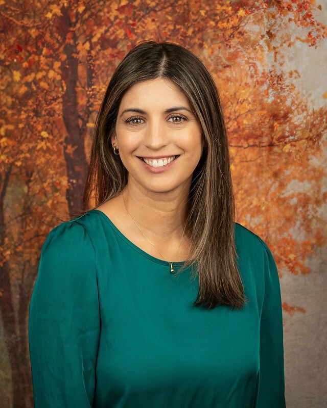 Smiling woman in a teal top against an autumn leaf backdrop