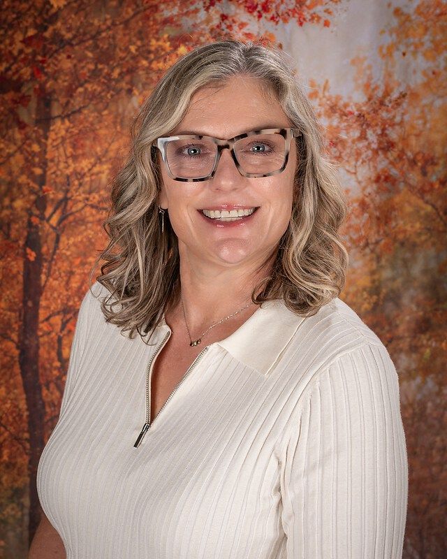 Woman smiling in glasses and white sweater against an autumn-leaf backdrop