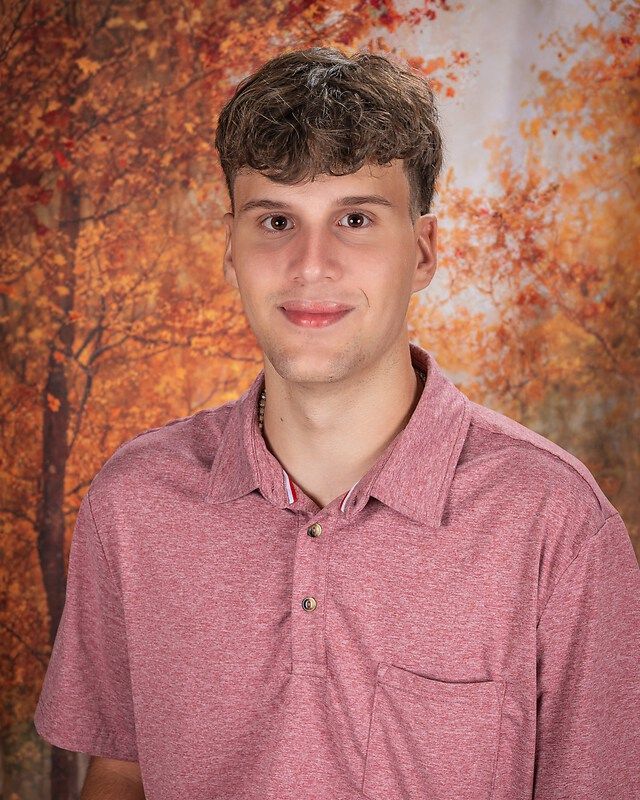 Young person in a red patterned shirt smiling against an autumn-toned backdrop