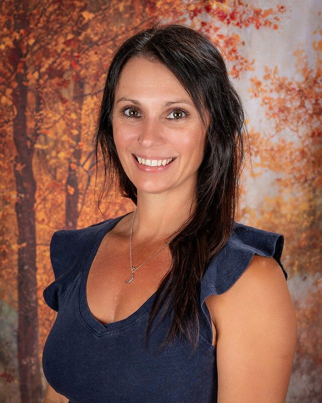 Smiling woman with dark hair in a navy top, posed against an autumn-toned backdrop.