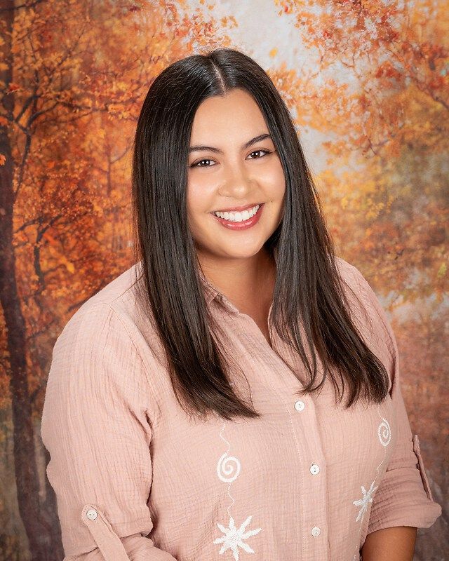 Smiling woman in a pink blouse against an autumn-colored backdrop