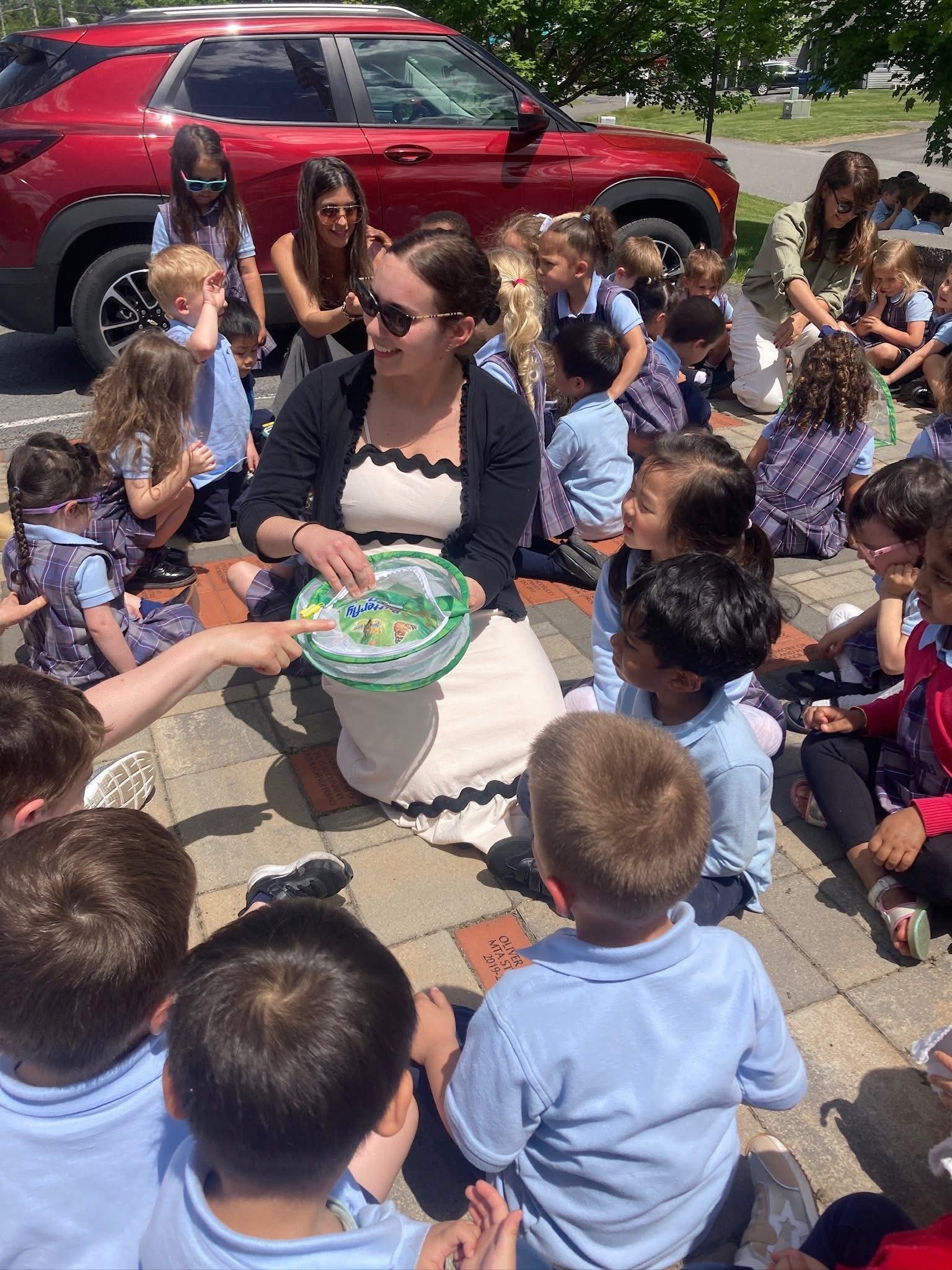 Teacher talking with child and parent at a table, with books, question marks, sun, clouds, and a house in the background