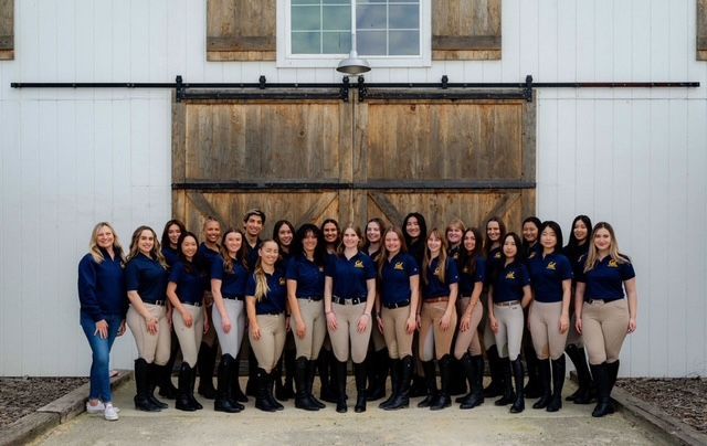 Group of people posing in front of a large wooden barn door, wearing matching dark shirts and tan pants.