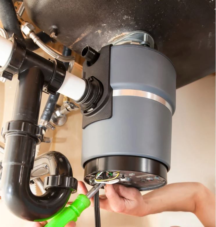 A person is fixing a garbage disposal with a green wrench