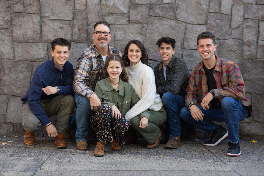 A family is posing for a picture in front of a stone wall.