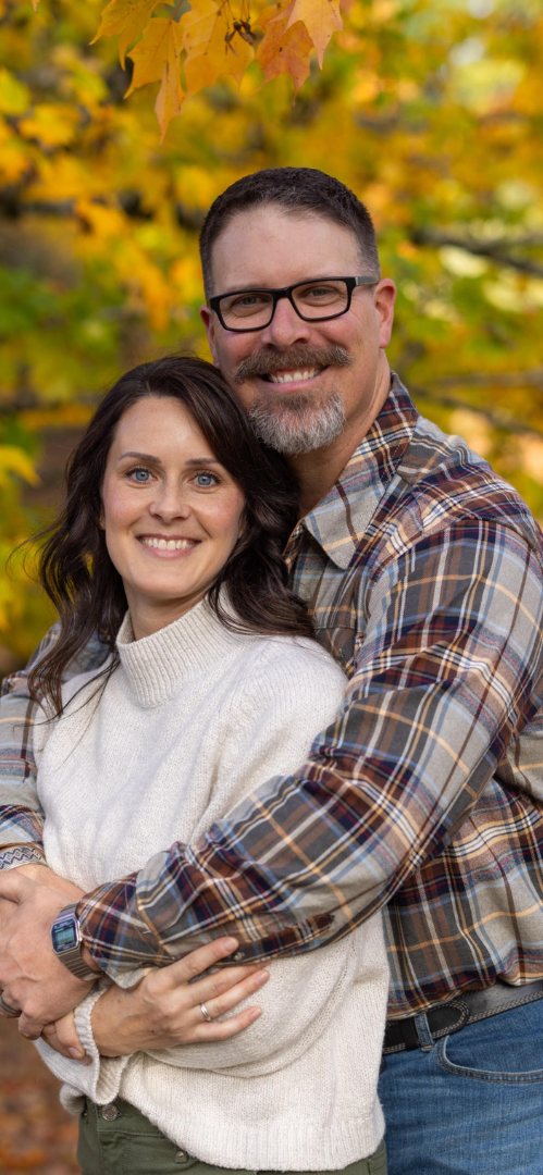 A man and a woman are hugging each other in front of a tree.