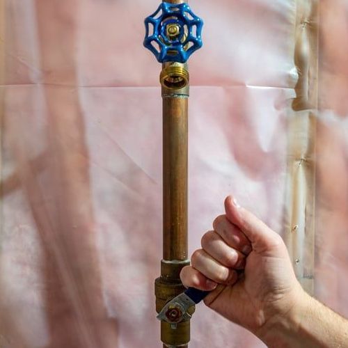 A person is holding a copper pipe with a blue valve on top.
