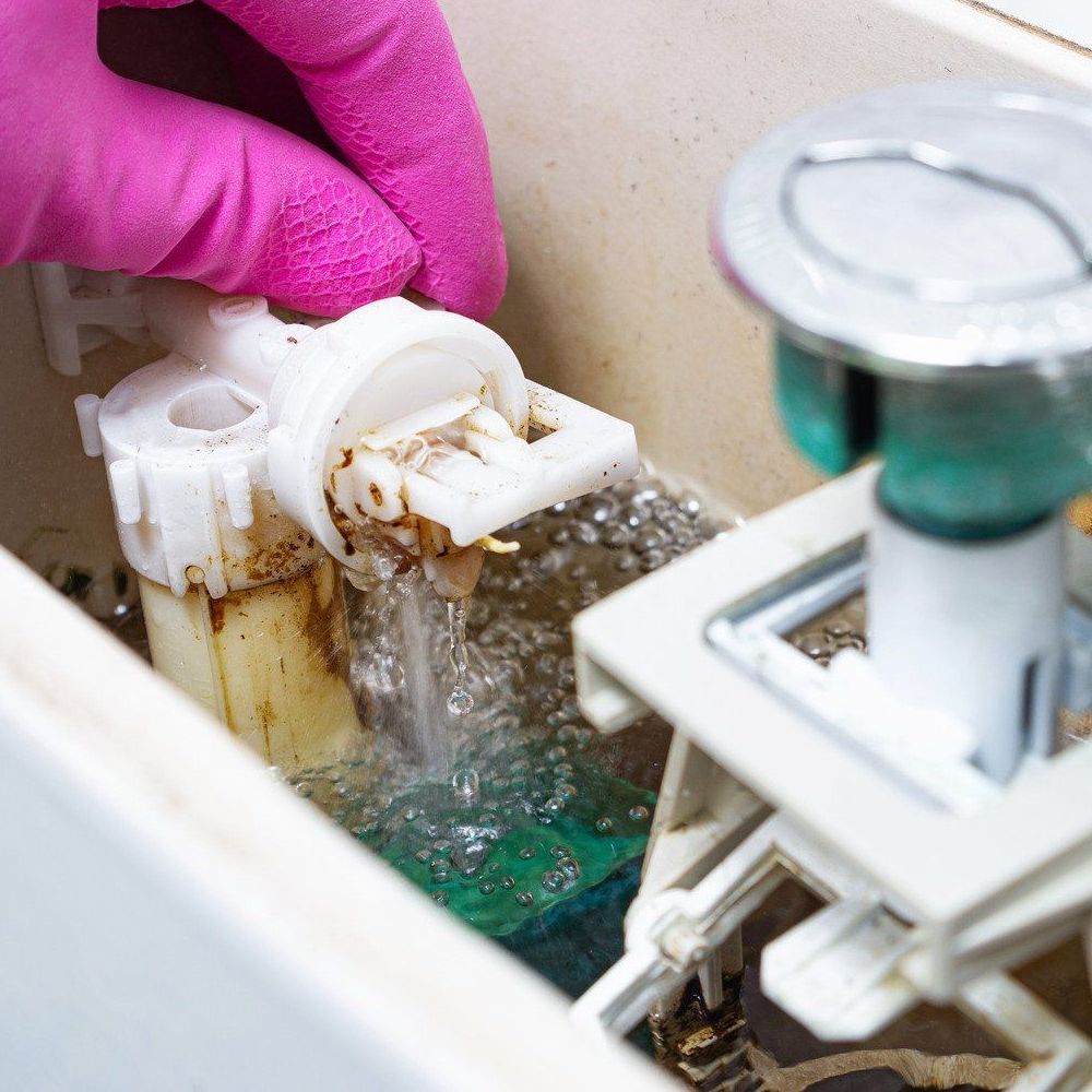 A person wearing pink gloves is cleaning a toilet tank