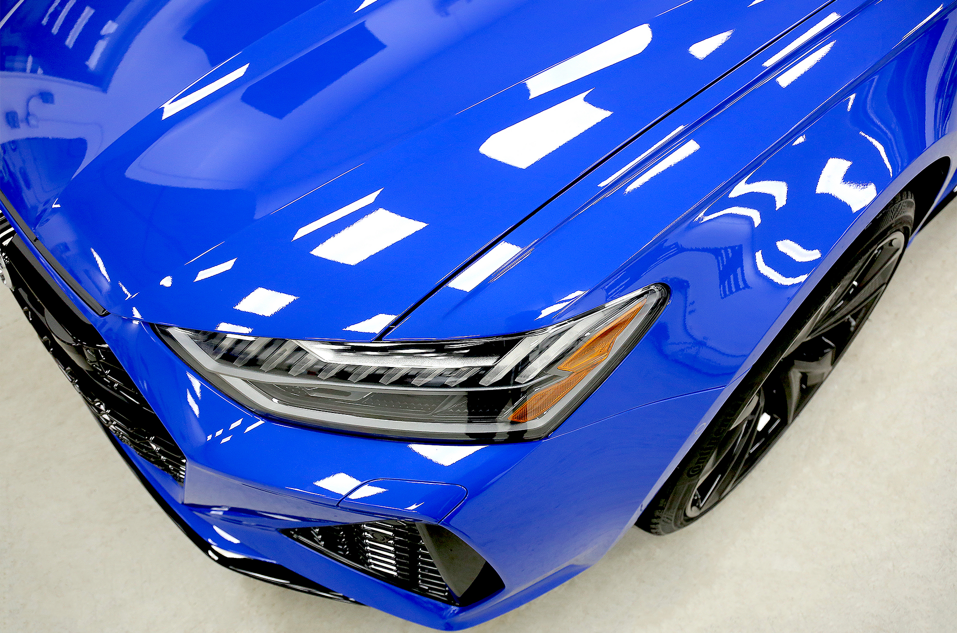 Close-up of a red car’s glossy hood and headlight with reflections
