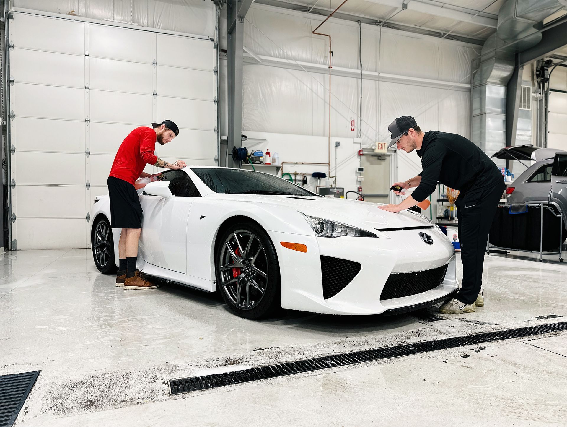 Two people cleaning a white Lexus LFA in a car detailing shop.