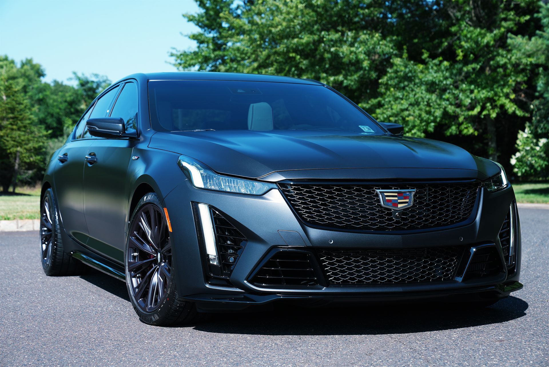 Black Cadillac sports sedan parked on pavement with trees in the background