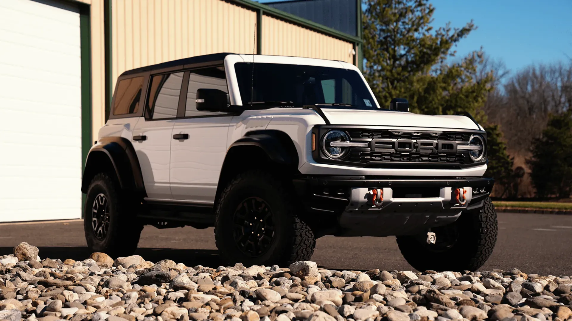 A white ford bronco raptor is parked in front of a garage.