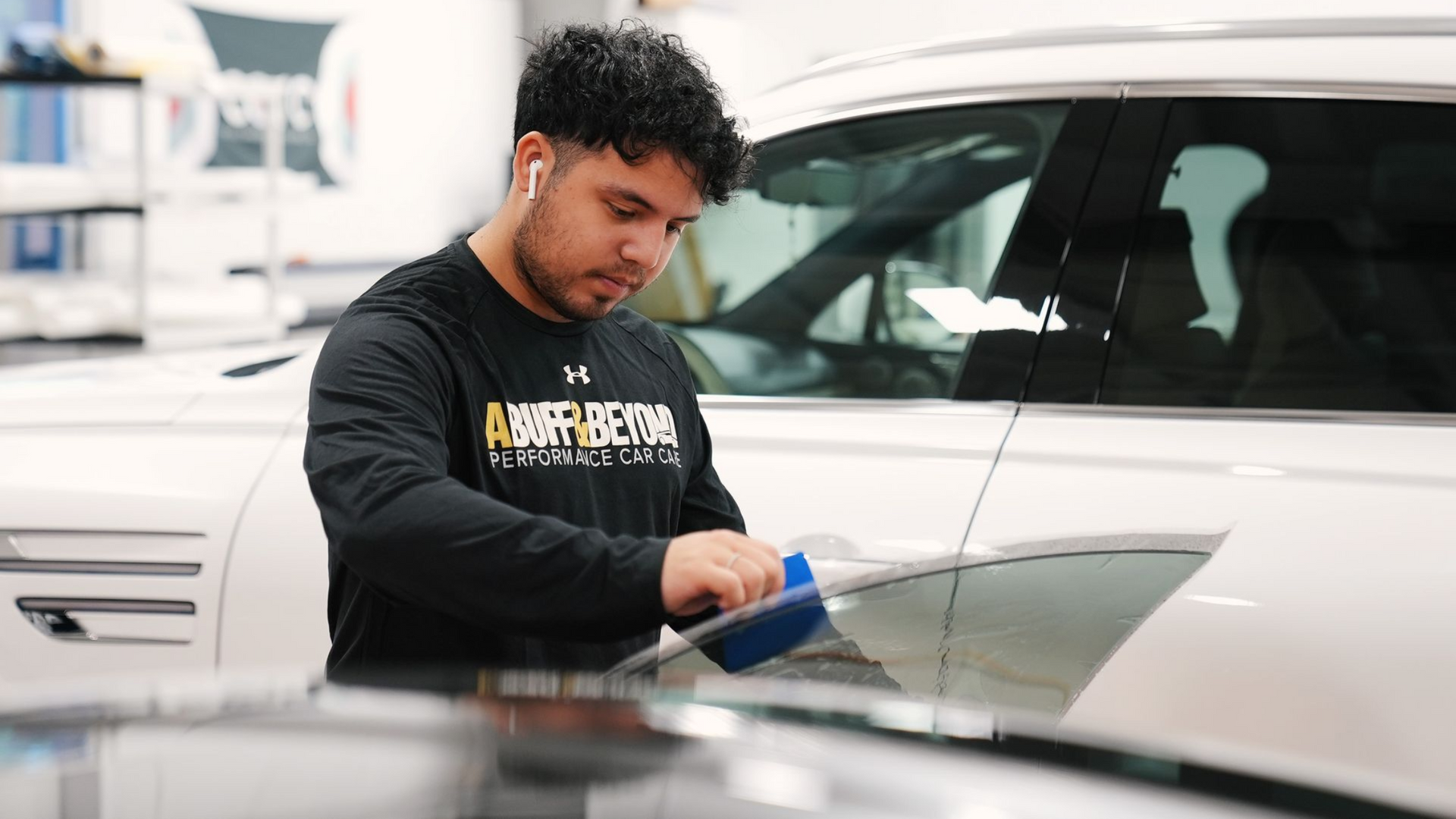 Man in a black shirt working on a car in a shop, using a blue applicator.