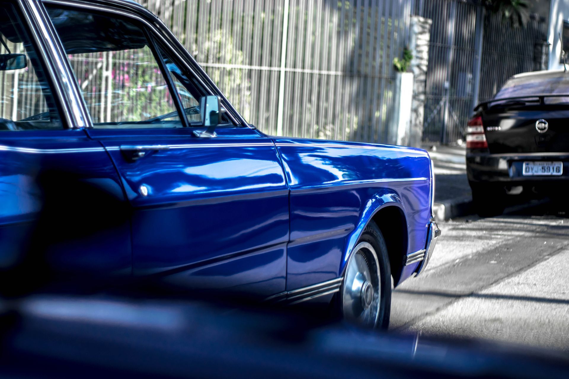 Blue classic car parked on a sunlit street with a black car behind it