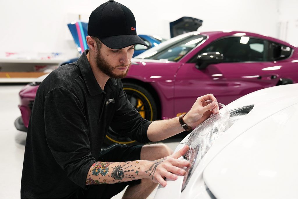 A man is wrapping a purple car in a garage.