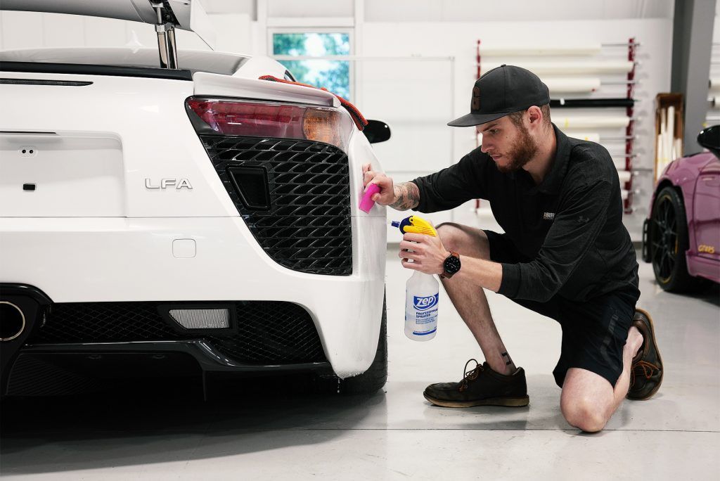A man is kneeling down next to a white car in a garage.