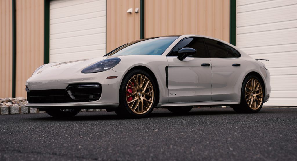A white porsche panamera is parked in front of a garage door.