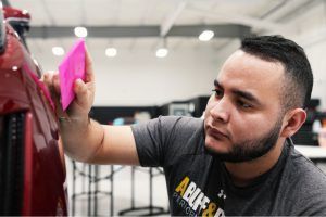 A man is using a pink spatula to polish a red car.