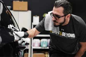 A man is cleaning a black car with a towel.