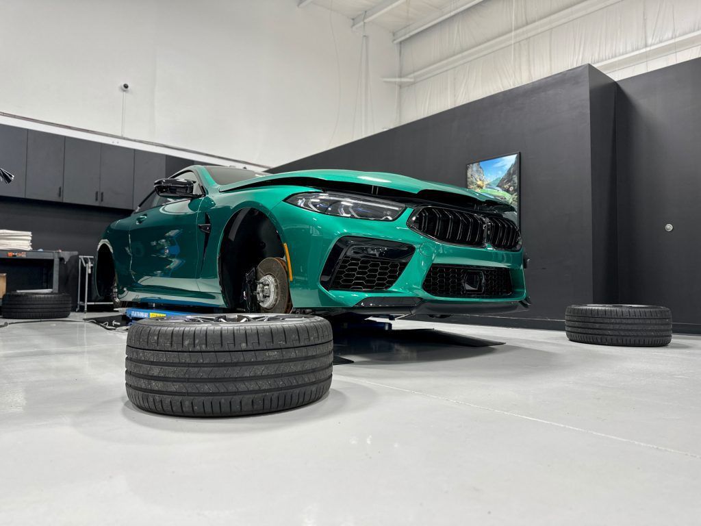 A green bmw m8 is sitting on top of a pile of tires in a garage.