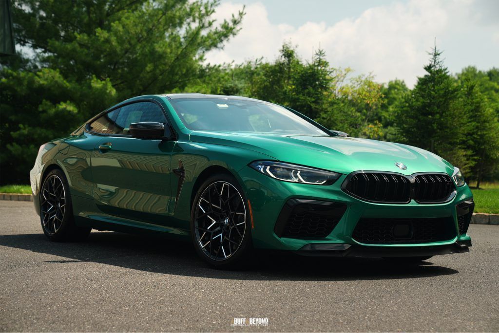A green bmw m8 coupe is parked on the side of the road.
