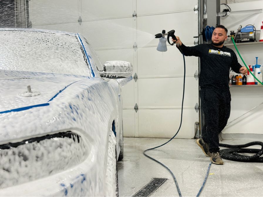 A man is washing a car with foam in a garage.