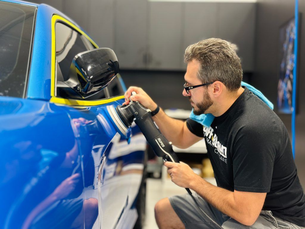 A man is polishing a blue car with a machine.