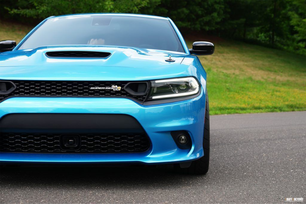 The front end of a blue dodge charger is parked on the side of the road.