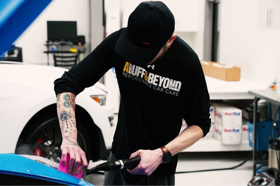 A man wearing a shirt that says auff beyond is polishing a car