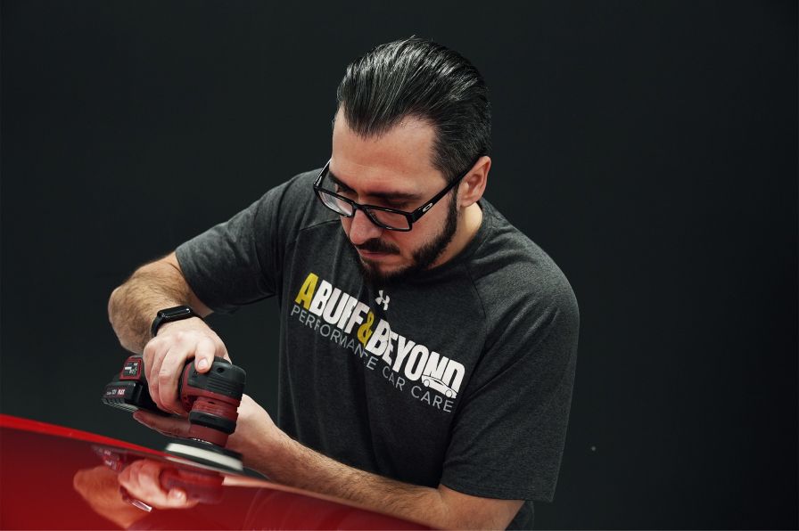A man is polishing a red car with a sander.