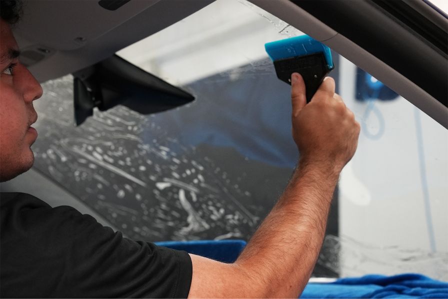 A man is applying tinted glass to the windshield of a car.