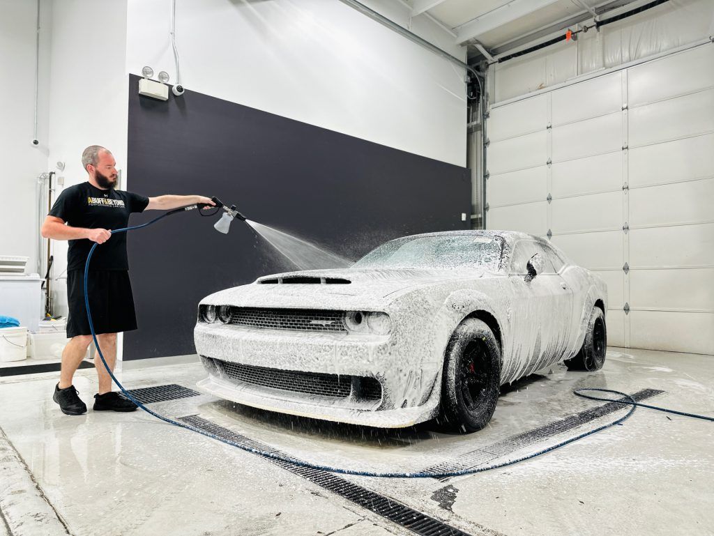 A man is washing a dodge challenger with foam in a garage.