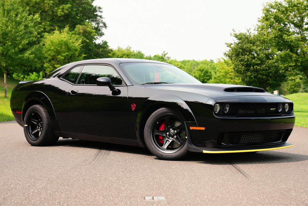 A black dodge challenger demon is parked on the side of the road.